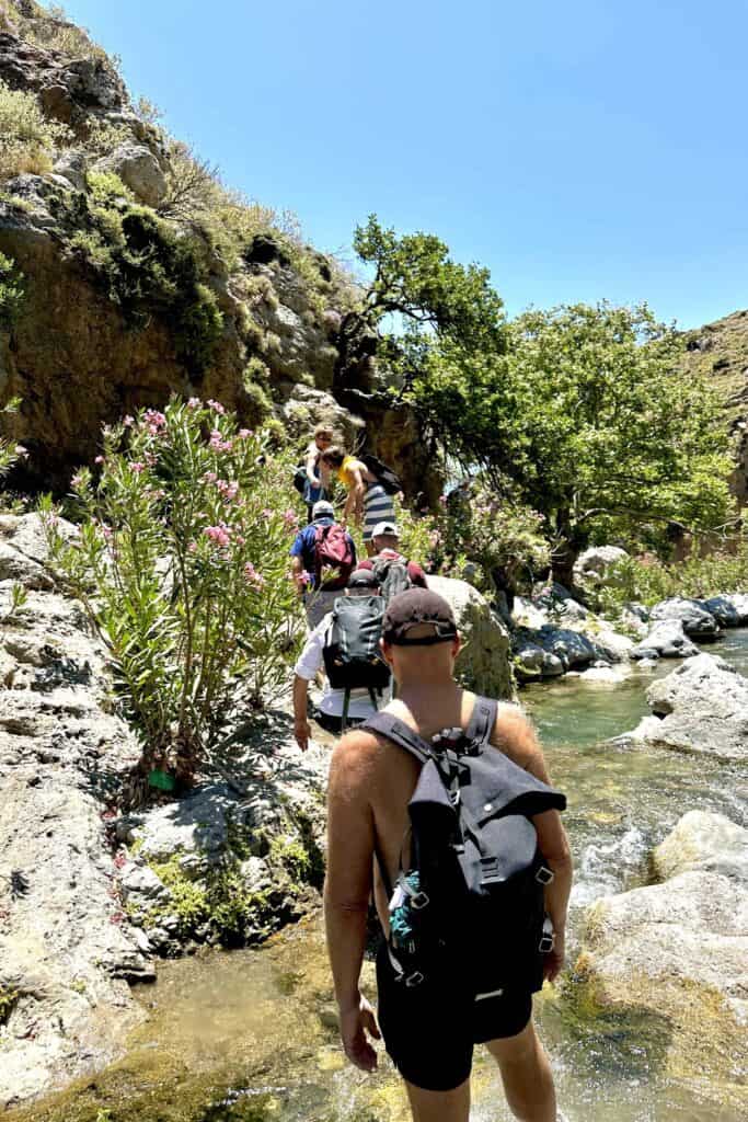 8-Day Group Retreat in Crete for Gay Men Hikers crossing a rocky stream in a scenic outdoor setting.